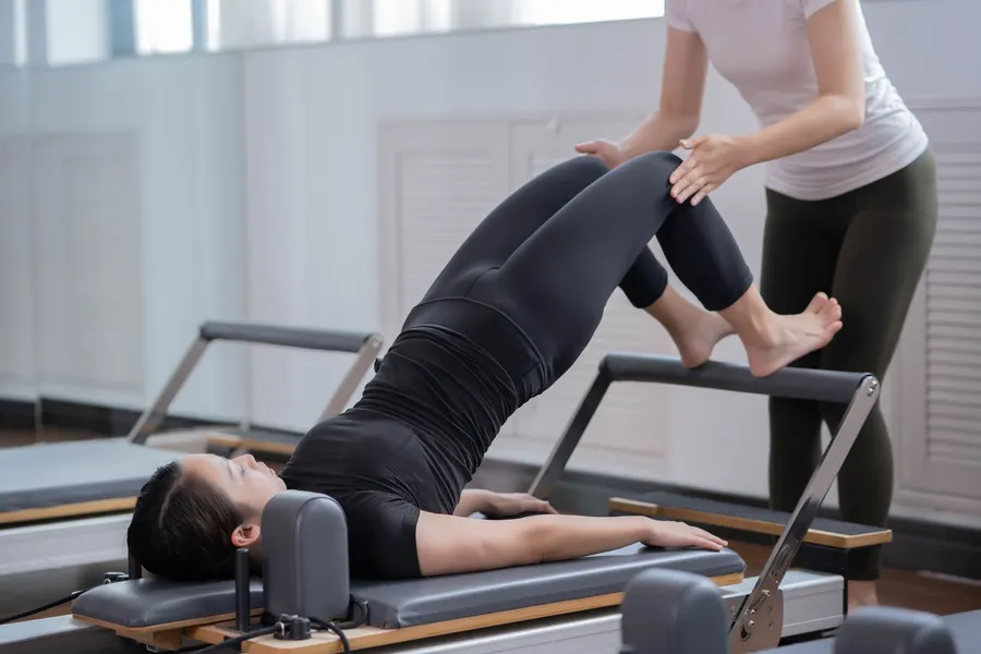 Profesora corrigiendo a una alumna en el reformer
